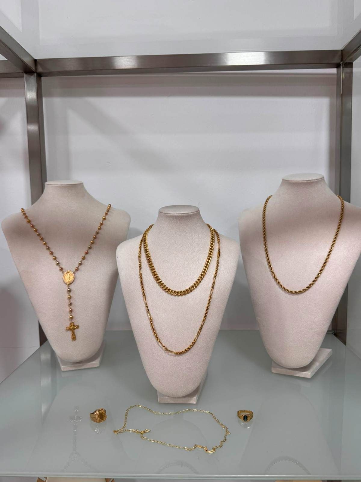 Tres collares de oro expuestos sobre soportes rosas en una vitrina de joyería.