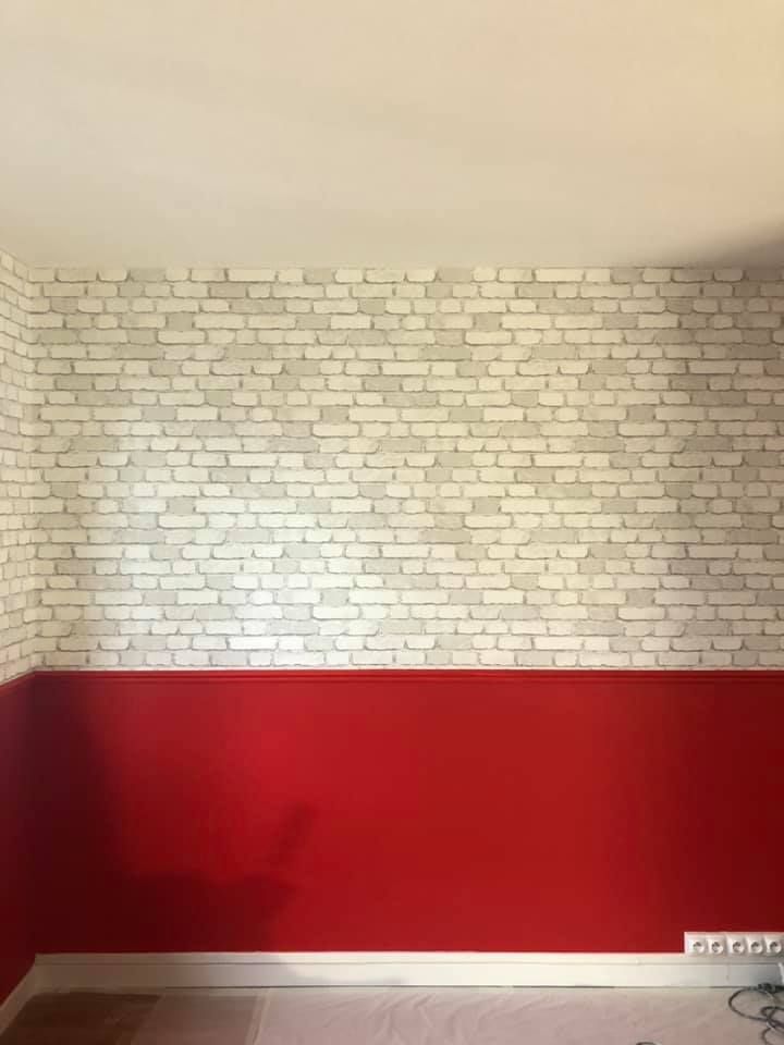 Mur peint en rouge en bas, papier peint à motifs de briques au-dessus ; plafond blanc.