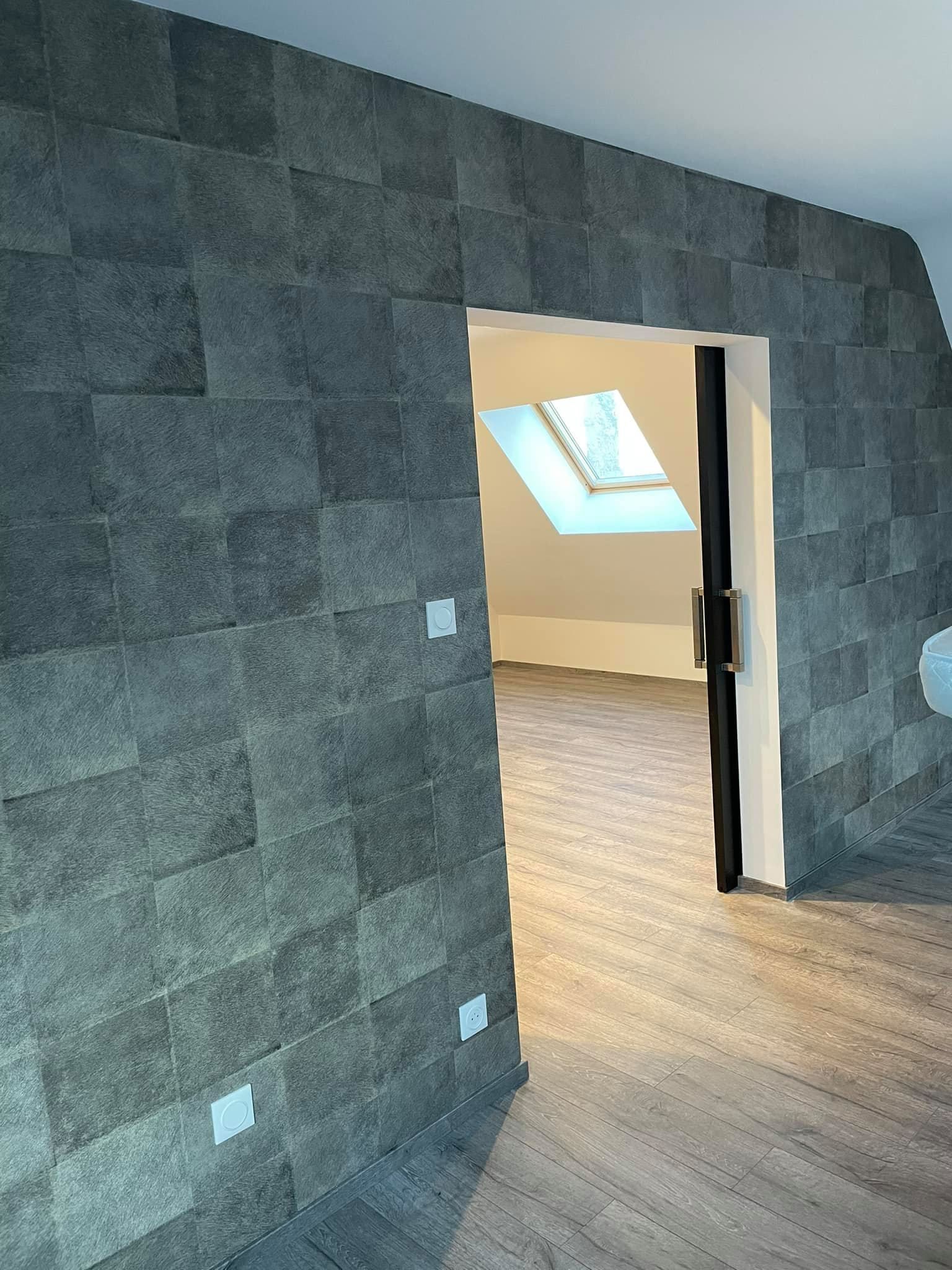 Mur carrelé en pierre avec une porte ouverte donnant sur une pièce dotée d'un puits de lumière, d'un parquet et de murs blancs.