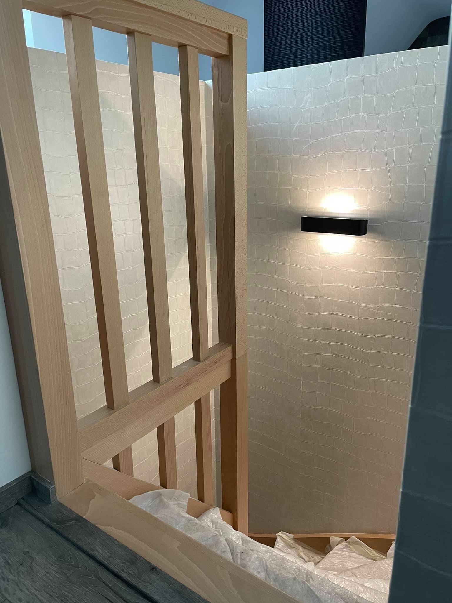 Cadre en bois appuyé contre un mur texturé avec un petit luminaire noir.