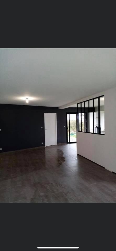 Intérieur d'une pièce avec parquet foncé, mur noir, porte blanche et grandes fenêtres à cadres noirs.