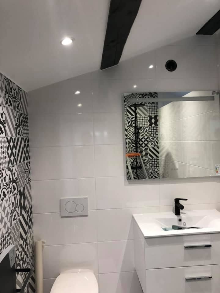 Salle de bains blanche avec carrelage à motifs, miroir, toilettes et robinet noir.