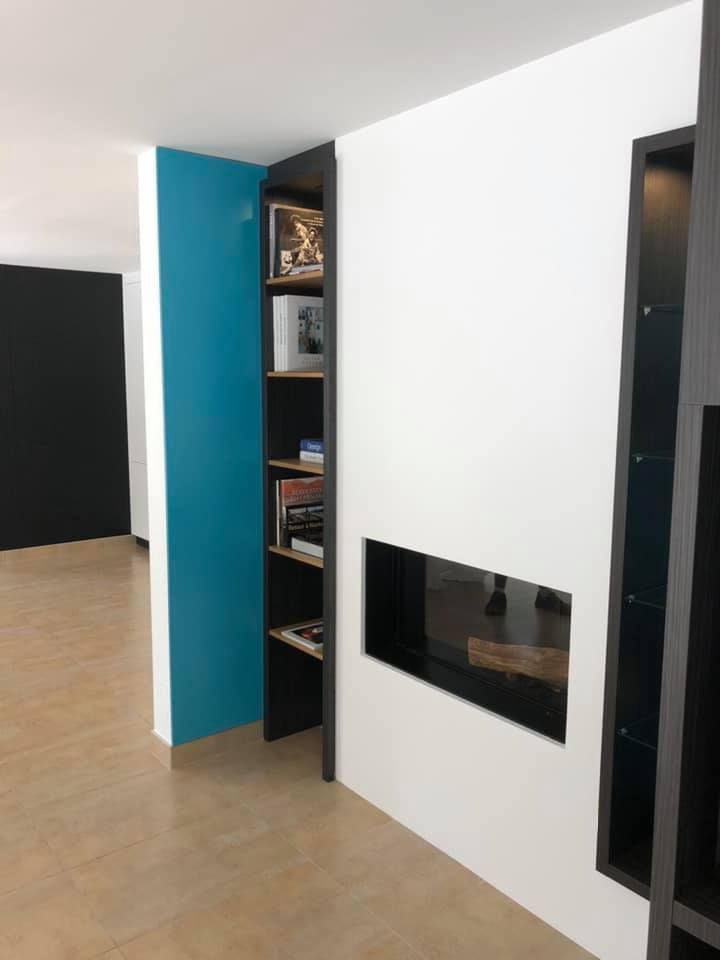 Étagères noires encastrées avec porte turquoise ouverte. Mur blanc avec cheminée encastrée. Sol beige.