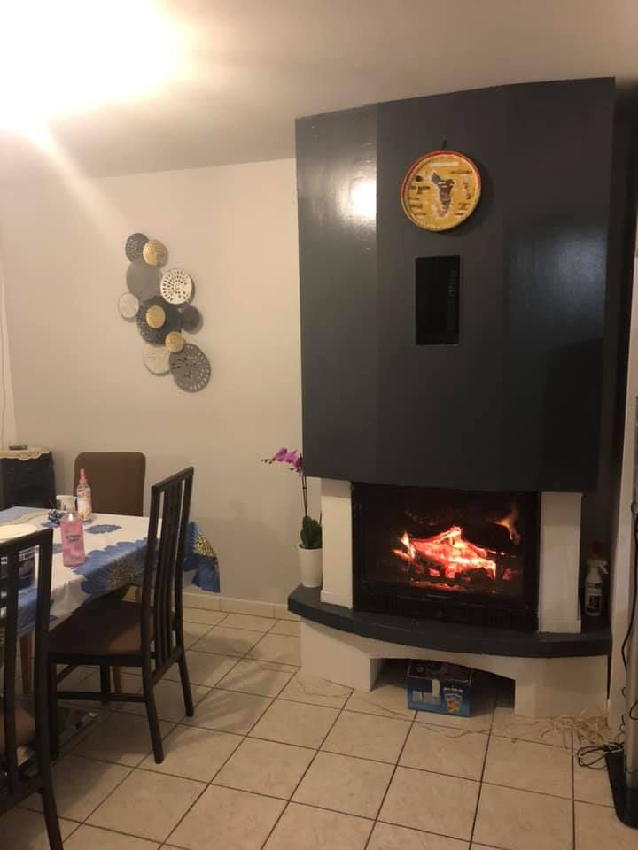 Cheminée avec feu allumé, horloge et table à manger dans une pièce confortable.