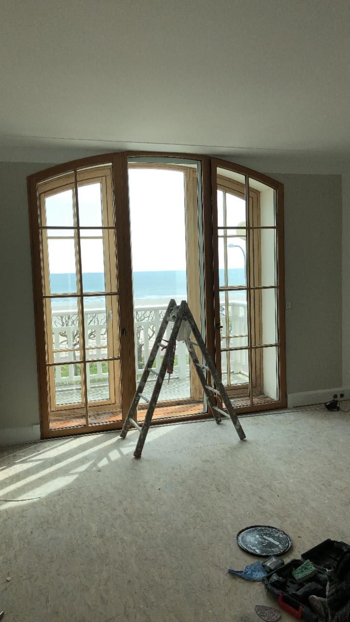 Vue intérieure d'une chambre avec des fenêtres incurvées et une échelle en façade, donnant sur un balcon et l'océan.