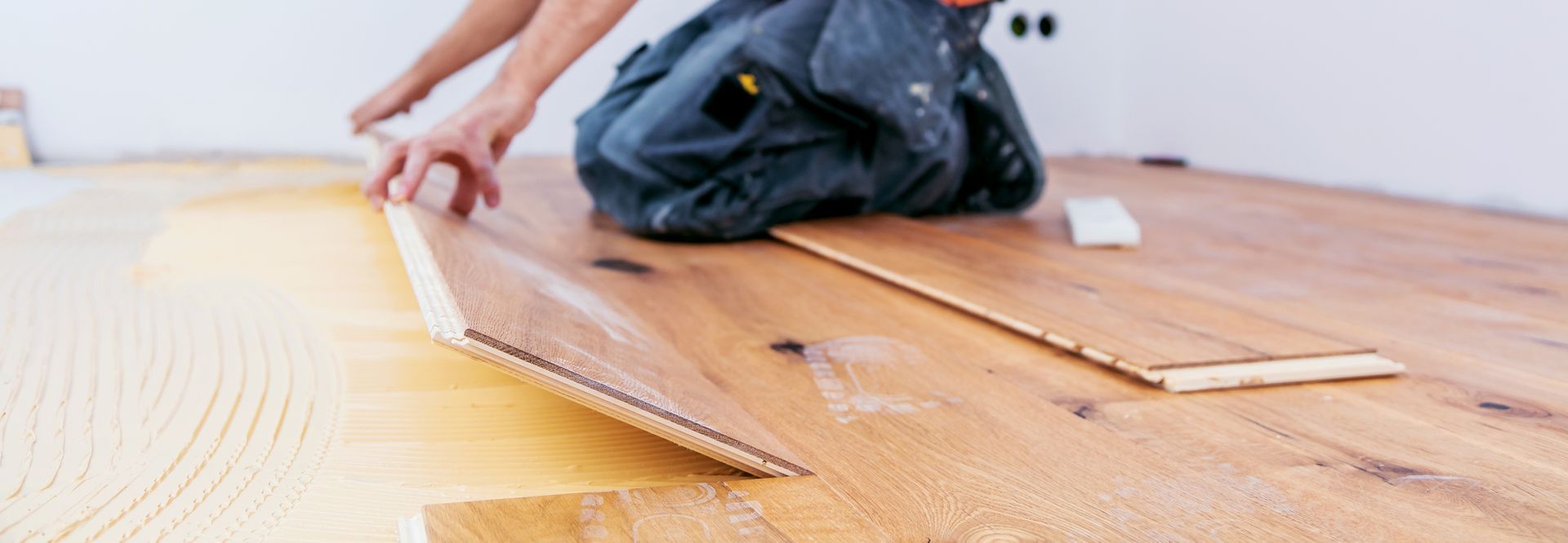 Une personne qui pose un parquet, applique la colle et ajuste les lames.