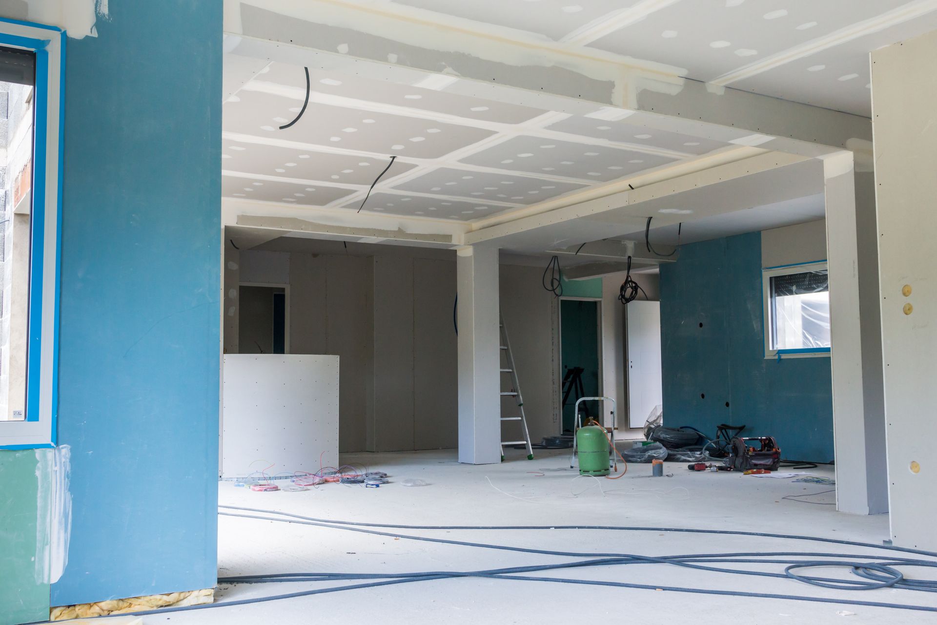 Espace intérieur en travaux ; cloisons sèches et murs peints en bleu, outils et câbles au sol.