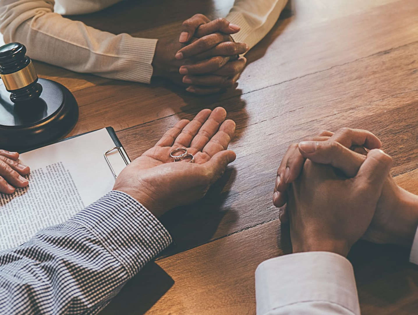 Une personne tient les alliances lors d'un règlement de divorce. D'autres personnes sont assises à une table avec un maillet et des documents.