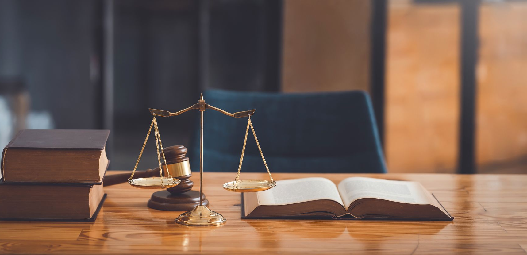 Une balance en or, un maillet et un livre ouvert sur un bureau en bois ; décor d'un cabinet d'avocats.
