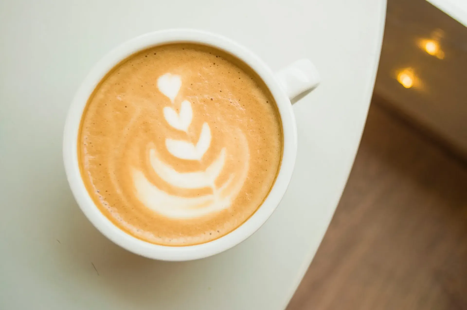 Café con leche decorado con espuma en forma de corazón en una taza blanca sobre una mesa.