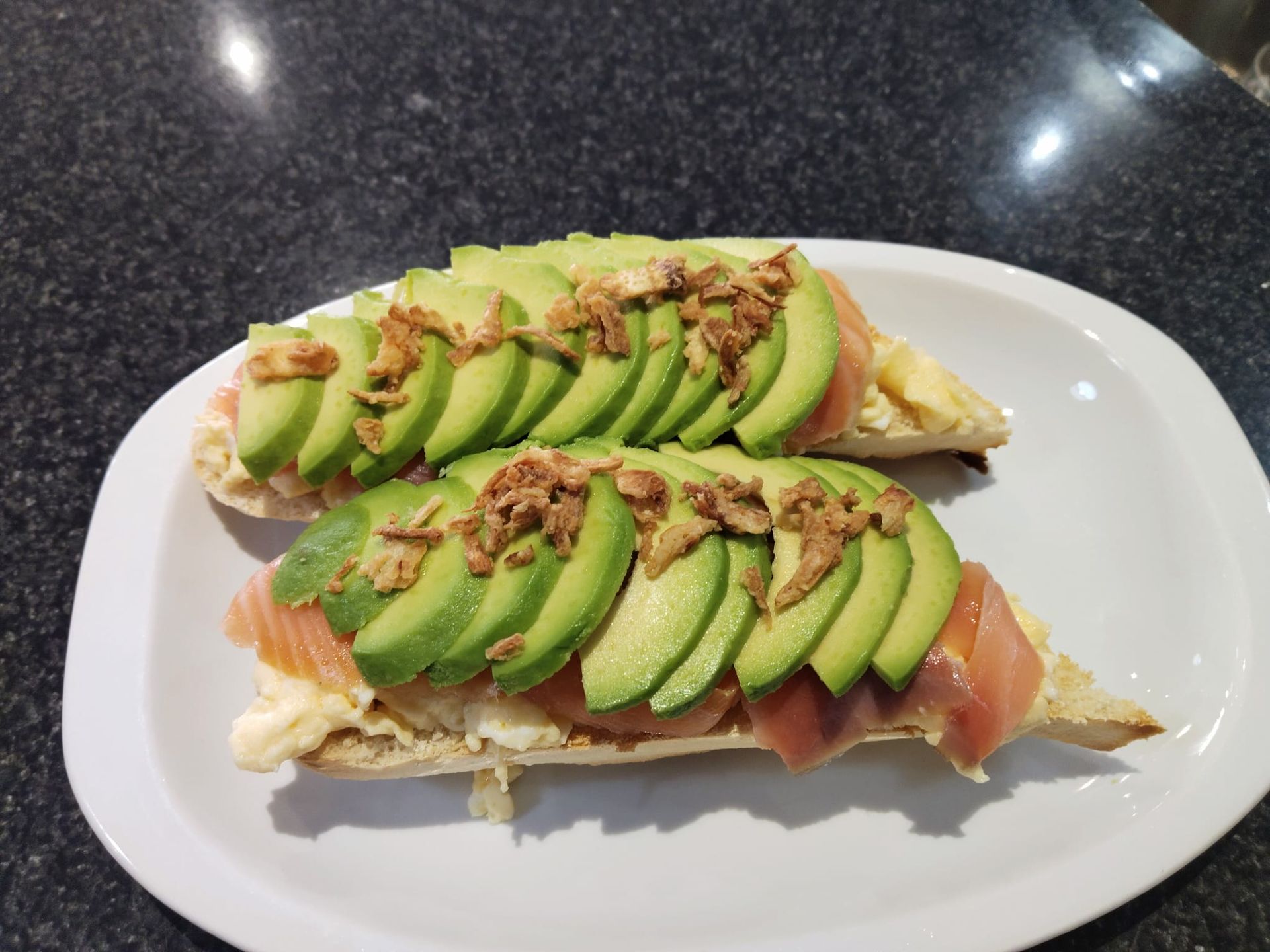 Huevos fritos con la yema líquida sobre tostada, acompañados de verduras, patatas fritas y chips en una tabla de madera.