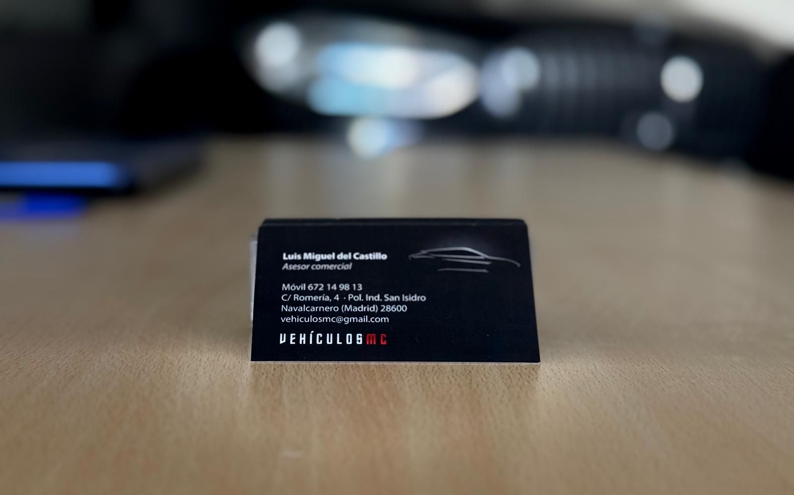 Tarjeta de presentación sobre una superficie de madera con el logotipo de un coche. Tarjeta negra con texto blanco.