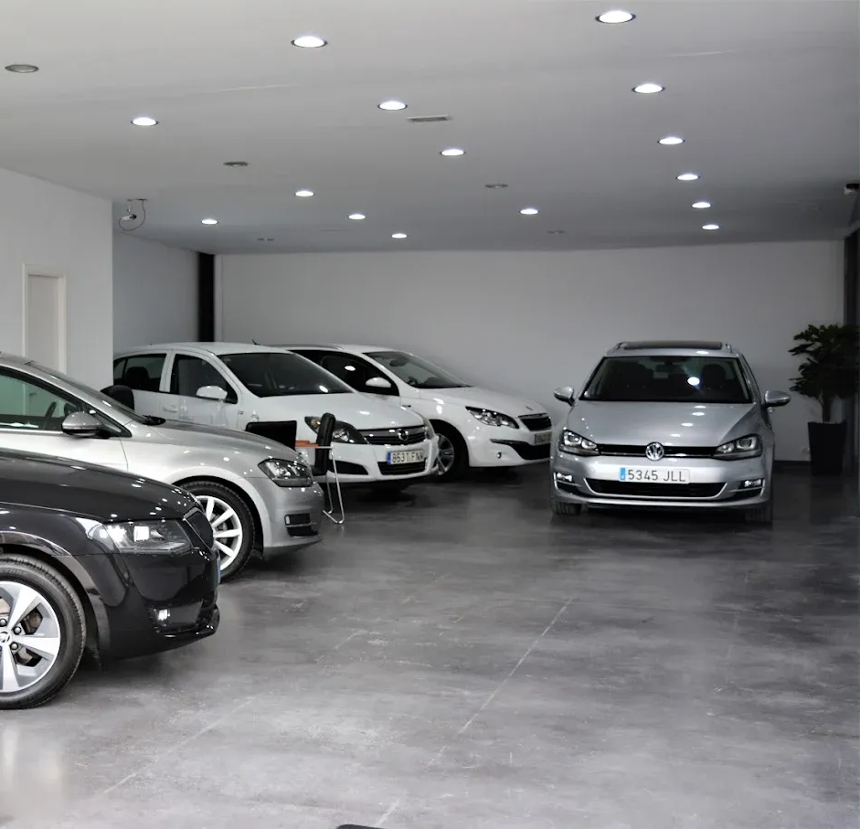 Autos exhibidos dentro de una sala de exposición moderna con paredes de vidrio e iluminación brillante.