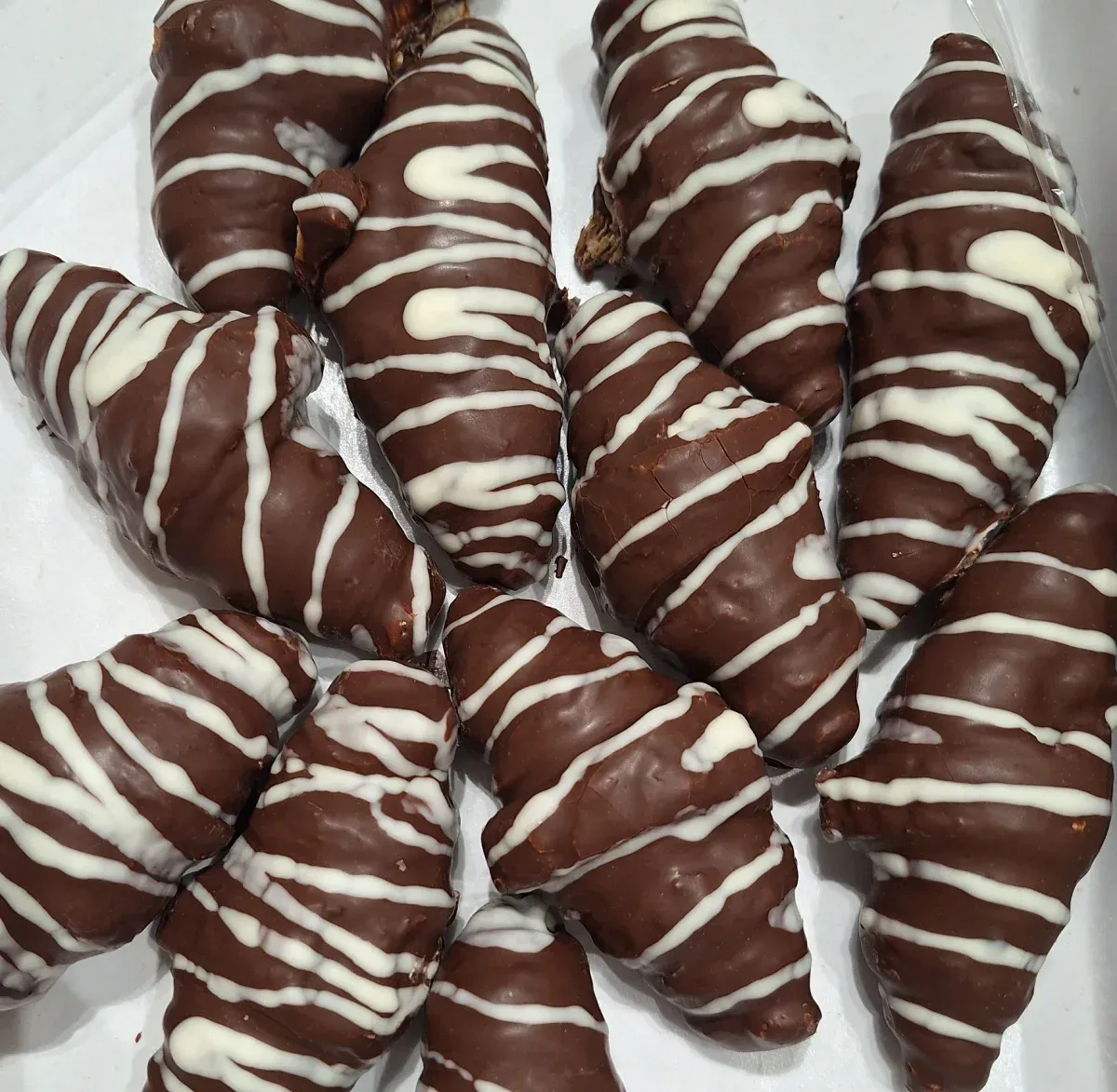Una caja de croissants cubiertos de chocolate con glaseado blanco.