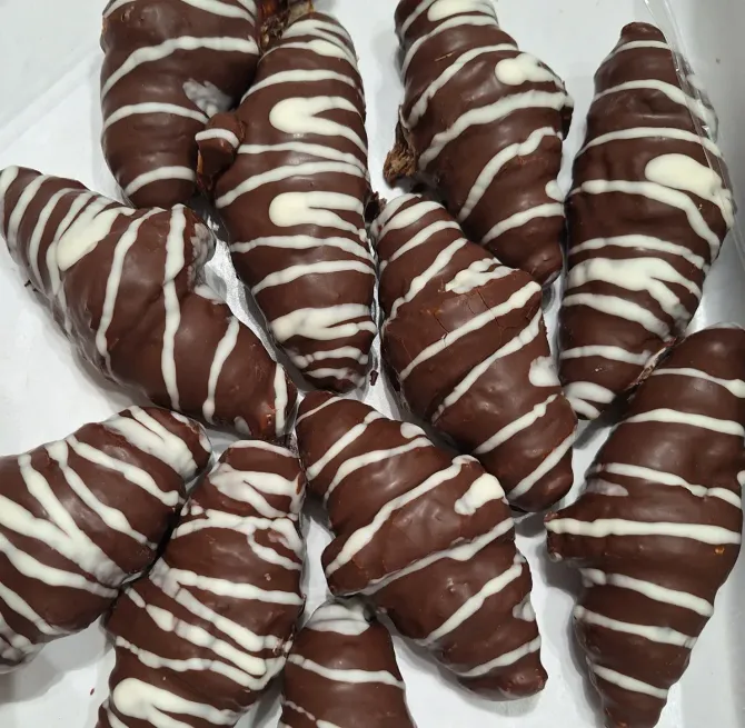Una caja de croissants cubiertos de chocolate con glaseado blanco.