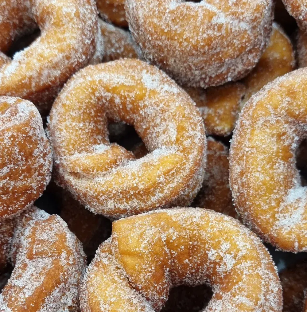 Primer plano de donas cubiertas de azúcar, apiladas, de color marrón dorado con cristales de azúcar blanco.