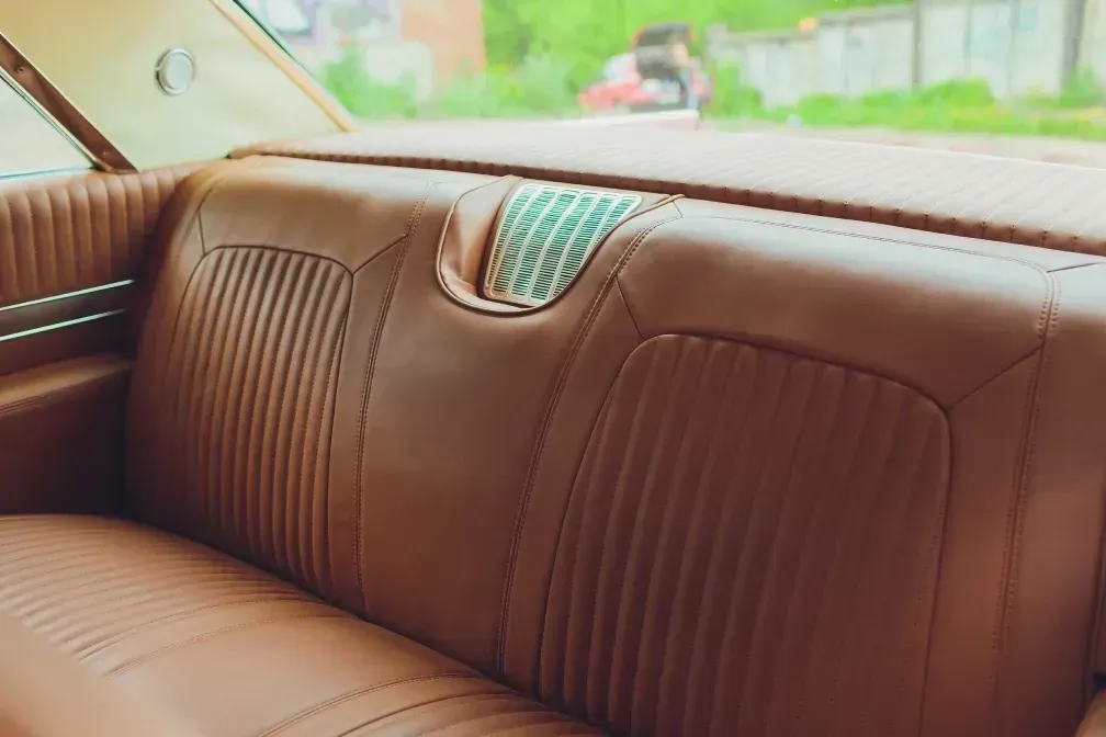 Asiento trasero de automóvil de cuero marrón con nervaduras verticales, detalles cromados y vista trasera.