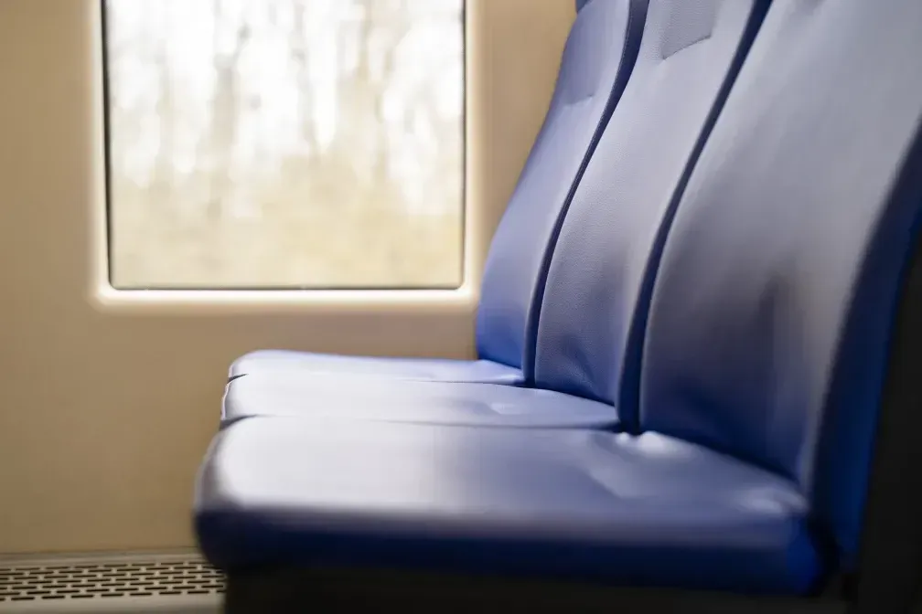 Asientos de tren azules junto a una ventana; vista borrosa del exterior.