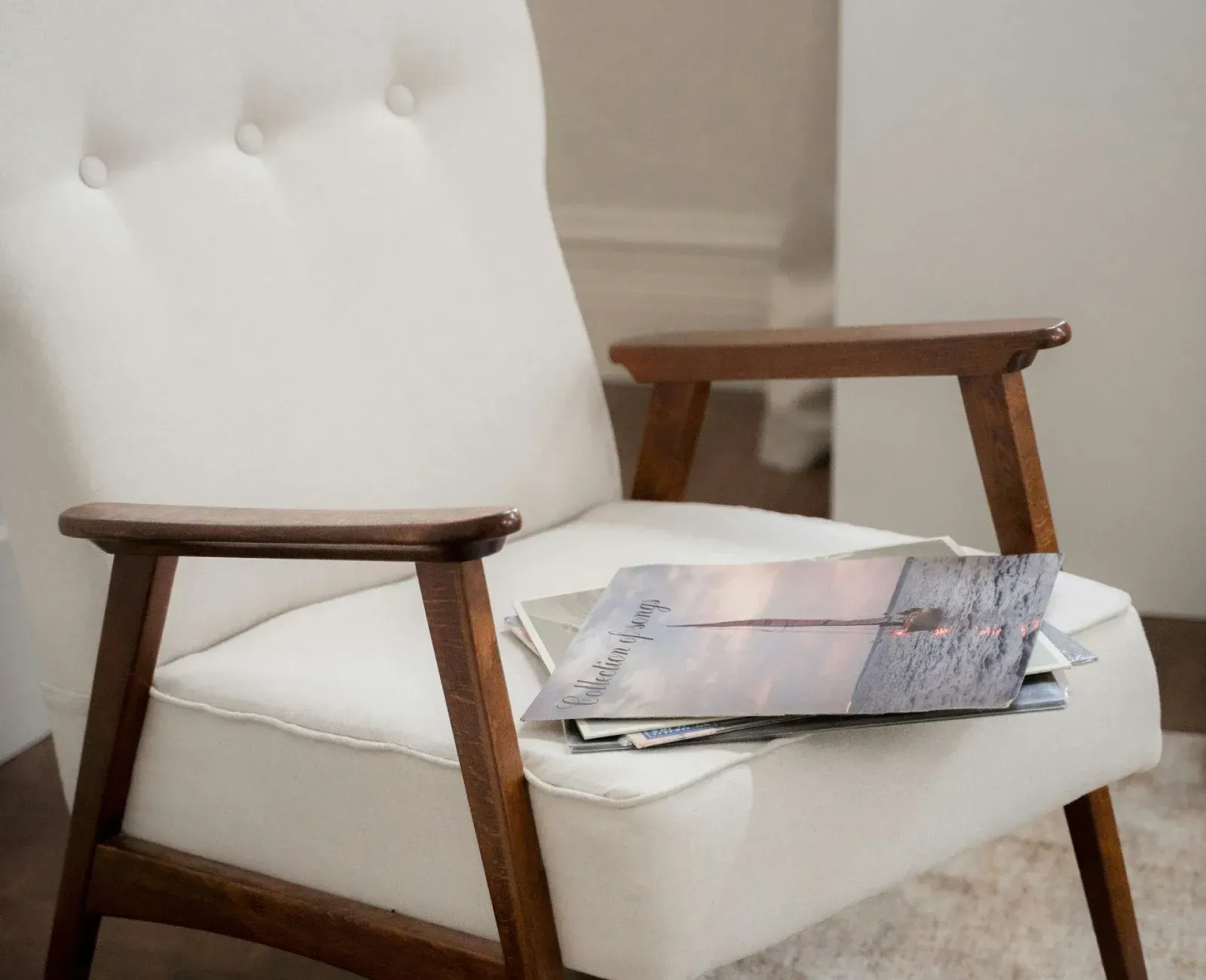 Silla tapizada en blanco con estructura de madera, que sostiene una pila de revistas.
