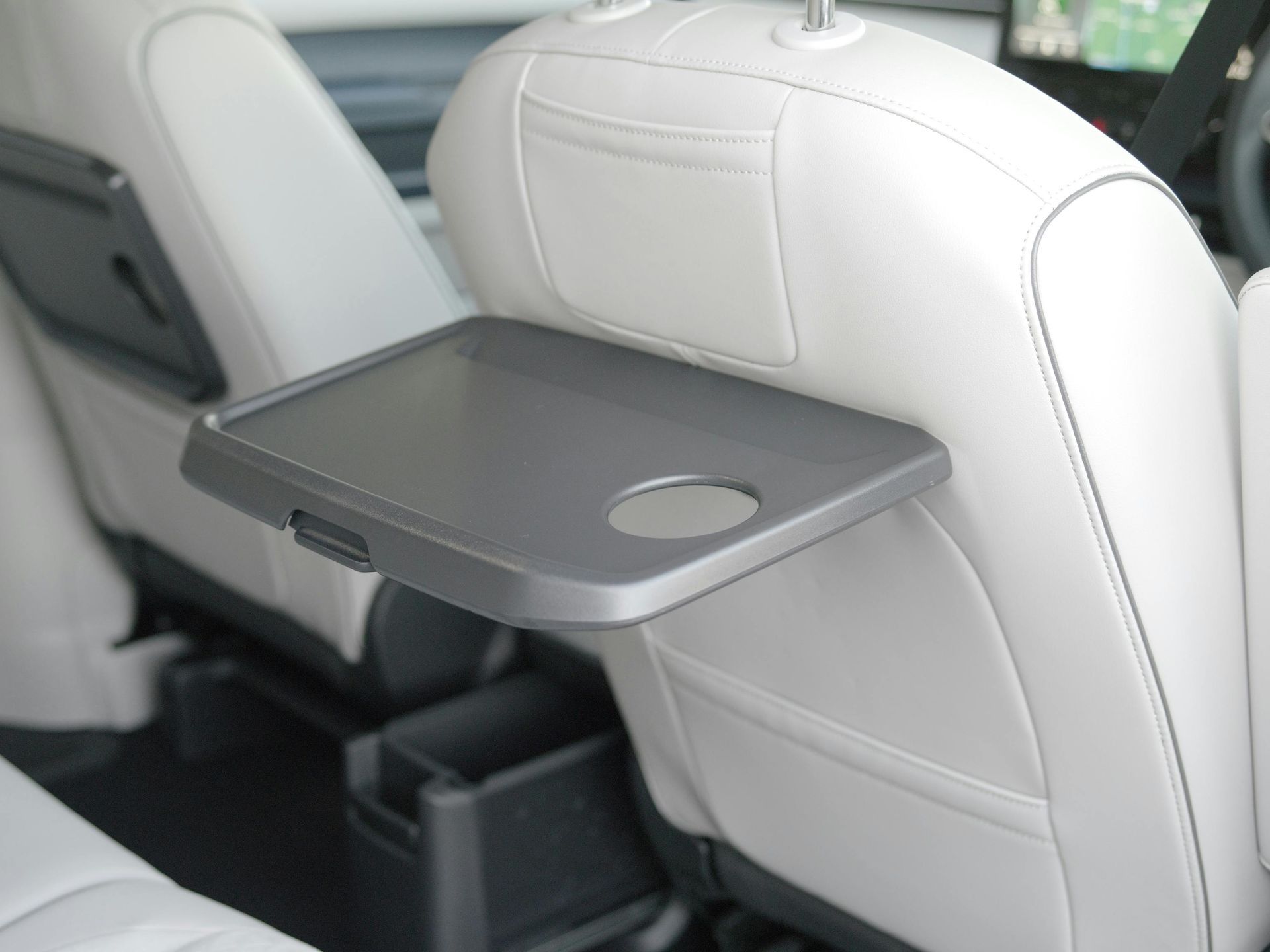 Mesa auxiliar gris plegada sobre un asiento de automóvil blanco, con portavasos.