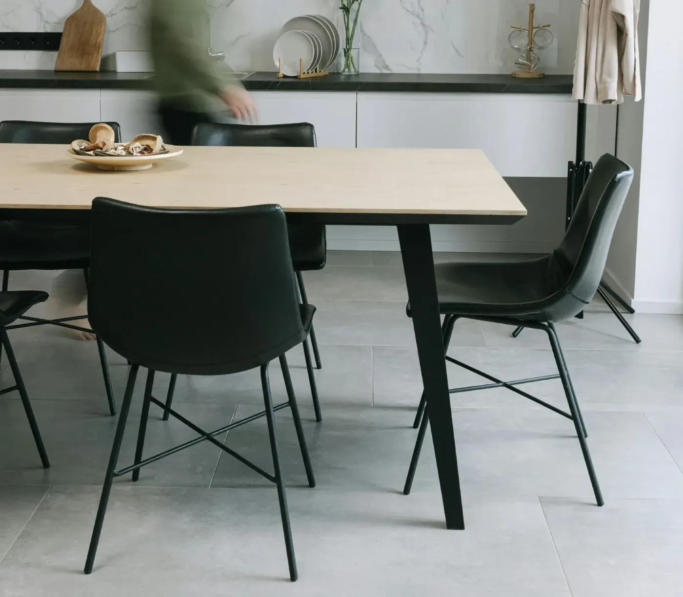 Mesa de comedor con sillas negras, persona al fondo, entorno de cocina.