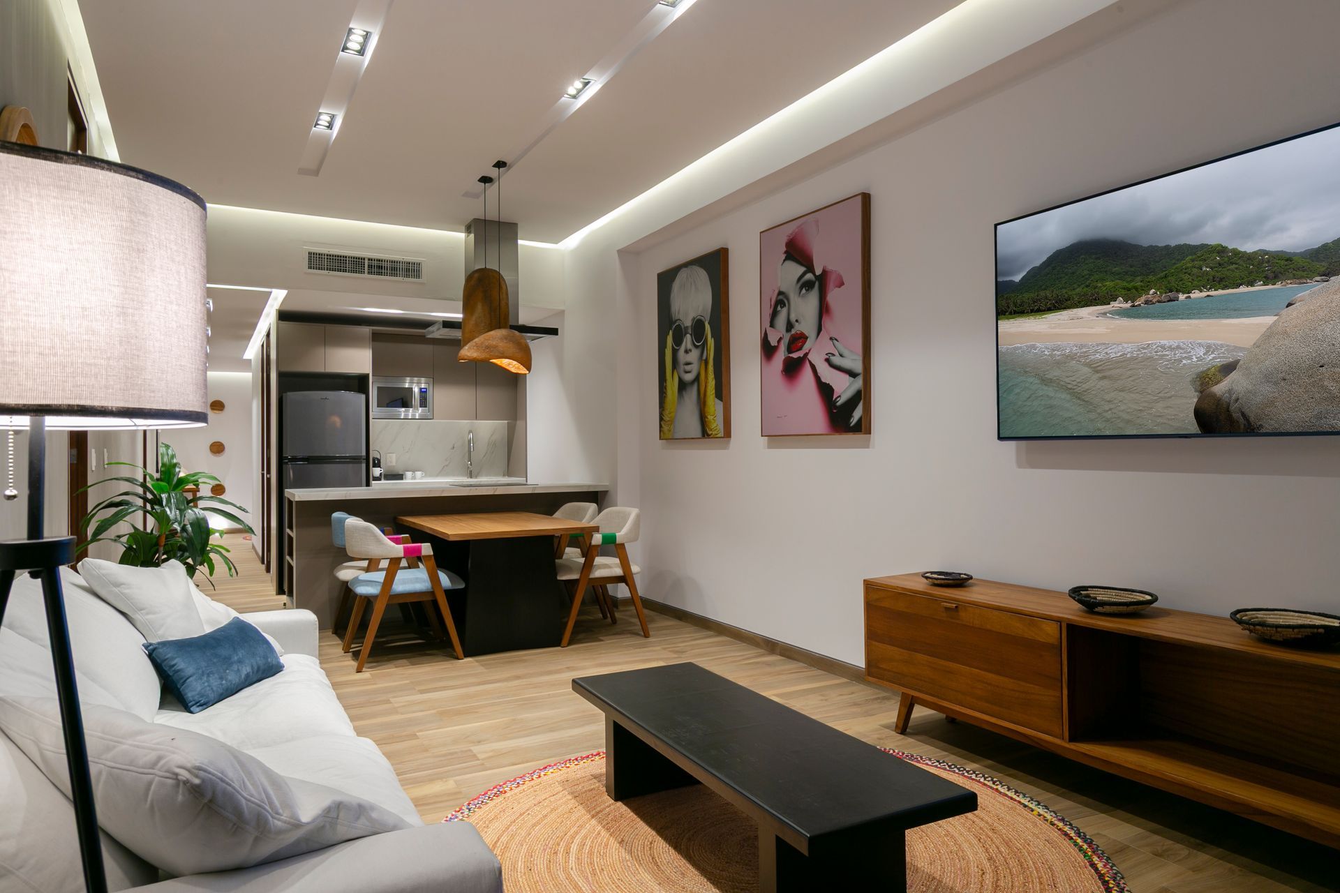 Modern living room with kitchen, art, TV, and wooden furniture.