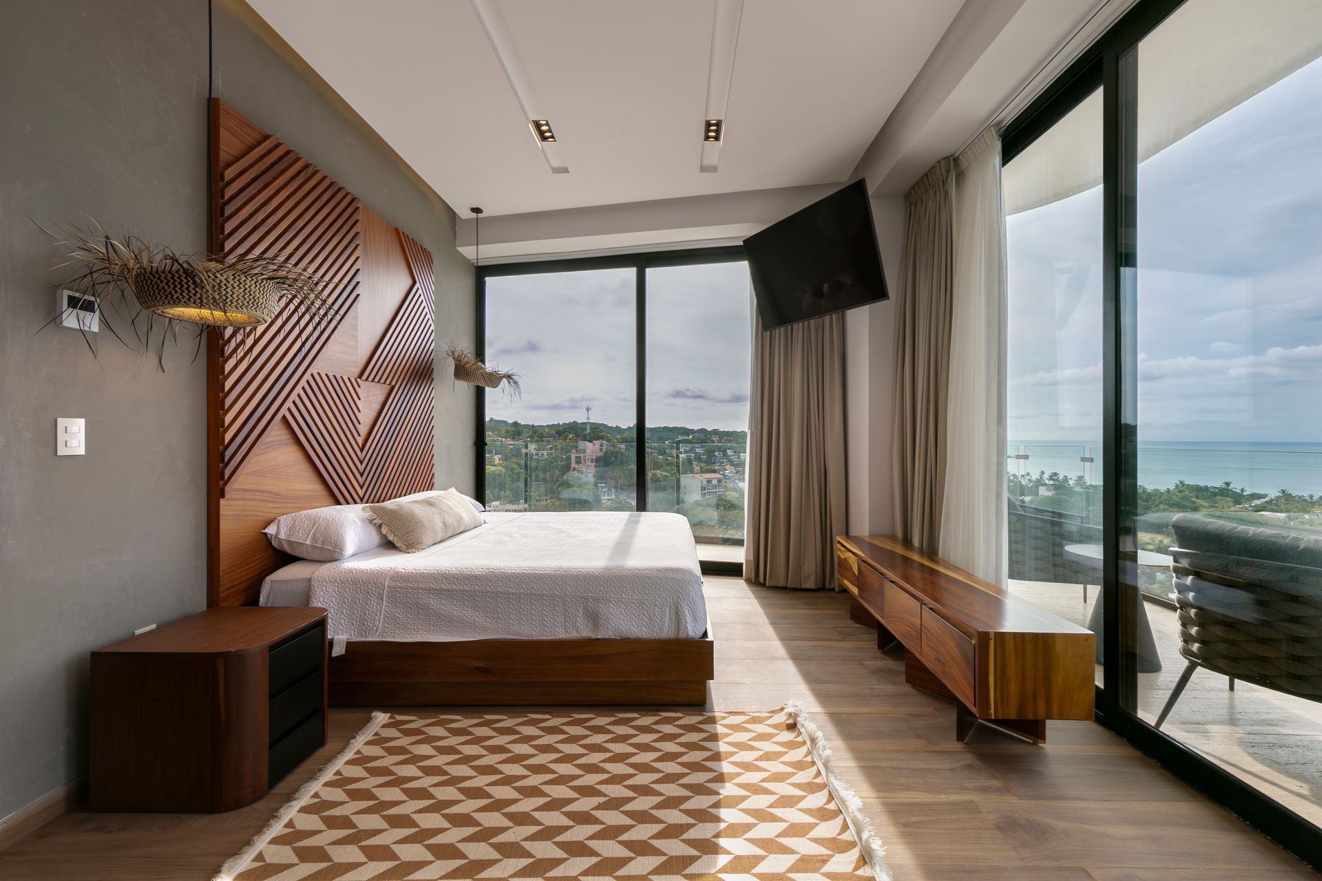 Modern bedroom with wooden headboard, large windows, and ocean view.