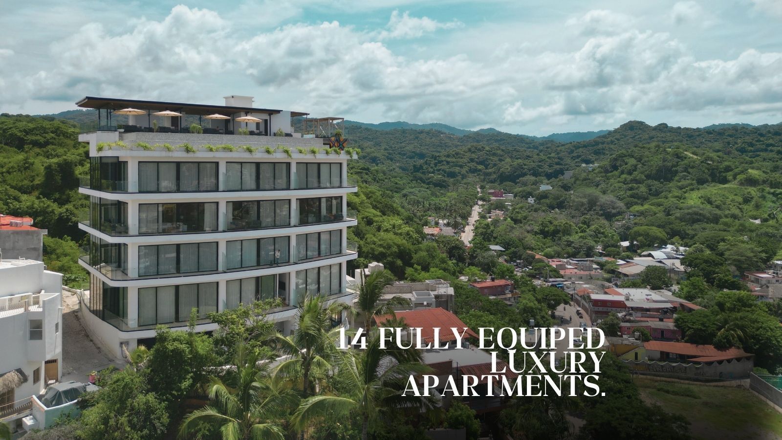 Modern apartment building on a hill with a view of a town and forest. Text reads: "14 Fully Equipped Luxury Apartments."