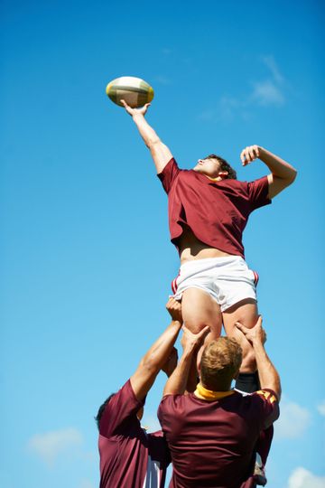 Un joueur de rugby est porté par ses coéquipiers pour récupérer le ballon de la touche