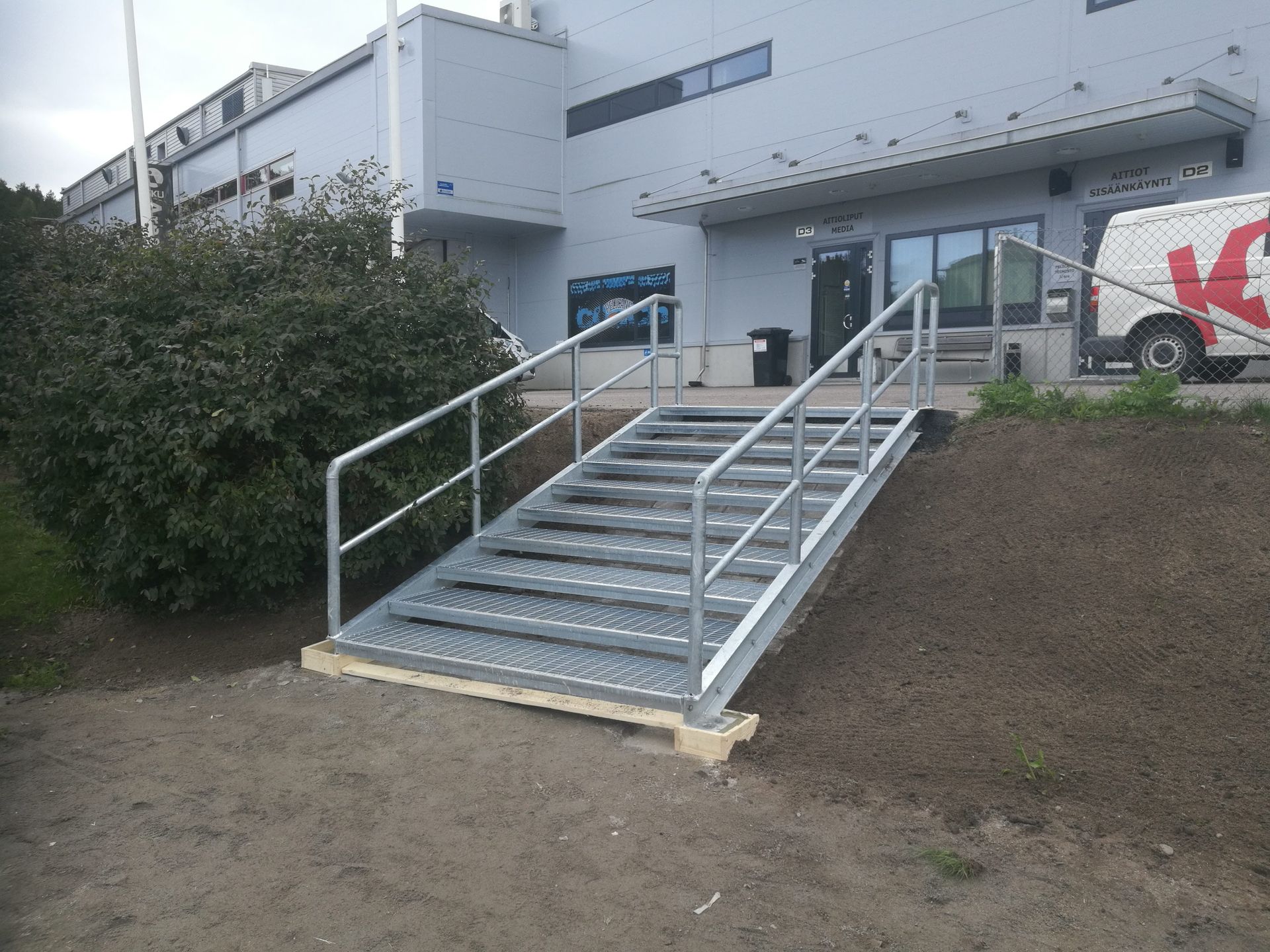 Metalliset portaat kaiteilla ylös valkoiselle rakennuksen sisäänkäynnille maarinteen vieressä.