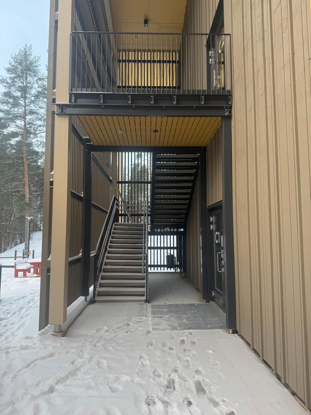 Ulkoportaikko ruskeiden rakennusten välissä, jossa on mustat metallikaiteet ja luminen maa