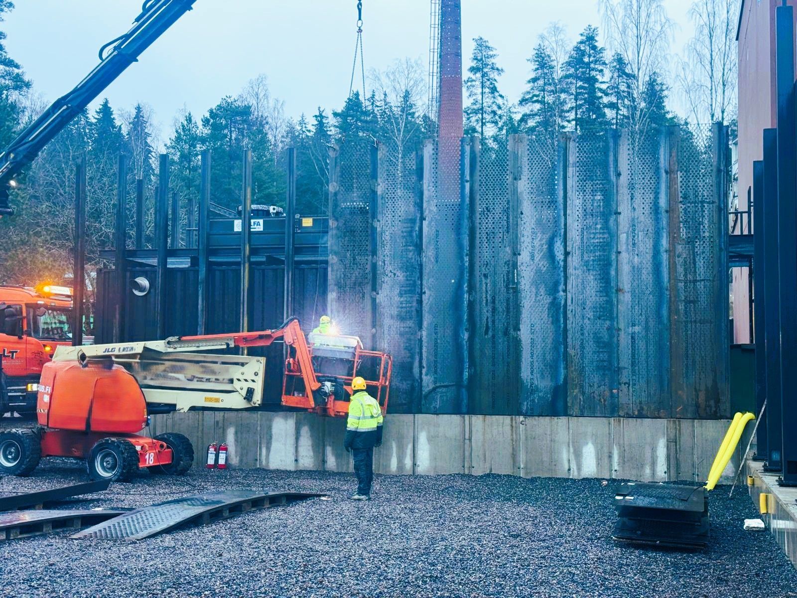Rakennustyöntekijät ja laitteet tienvarsityömaalla, jossa on betoniseiniä ja korkeita puita