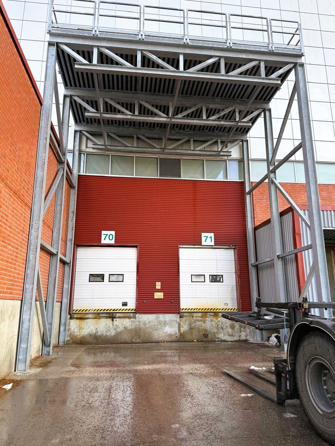 Teollisuuden lastauslaituri, jossa on punainen seinä, kaksi valkoista laituriluukkua ja kuorma-auto oikealla teräskatoksen alla