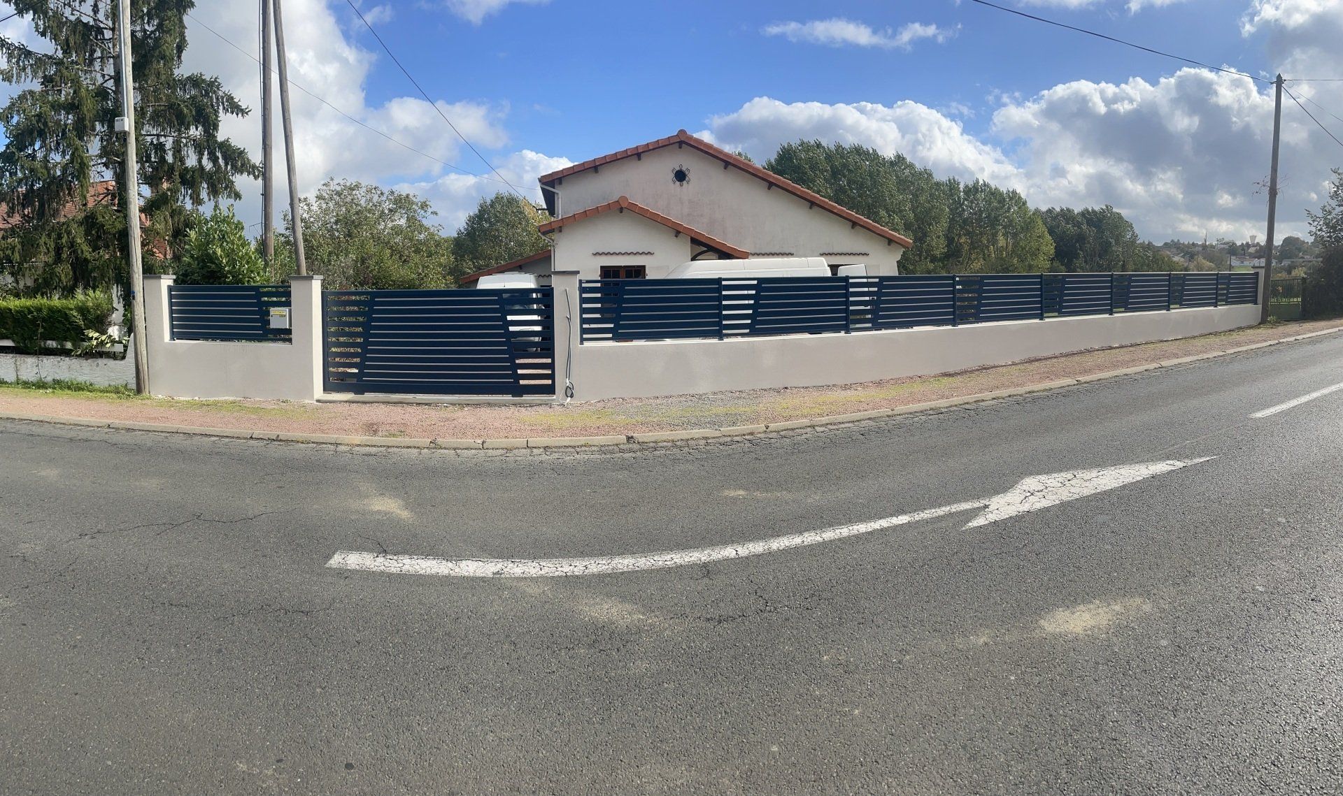 Maison de plain-pied avec une clôture en métal bleu au bord d'une route.
