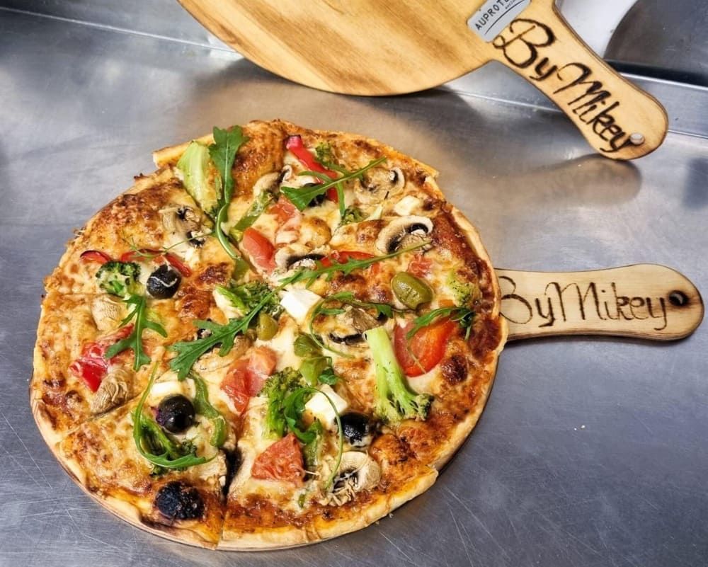 Eine Pizza liegt auf einem Holzbrett mit dem Namen by mikey darauf | By Mikey