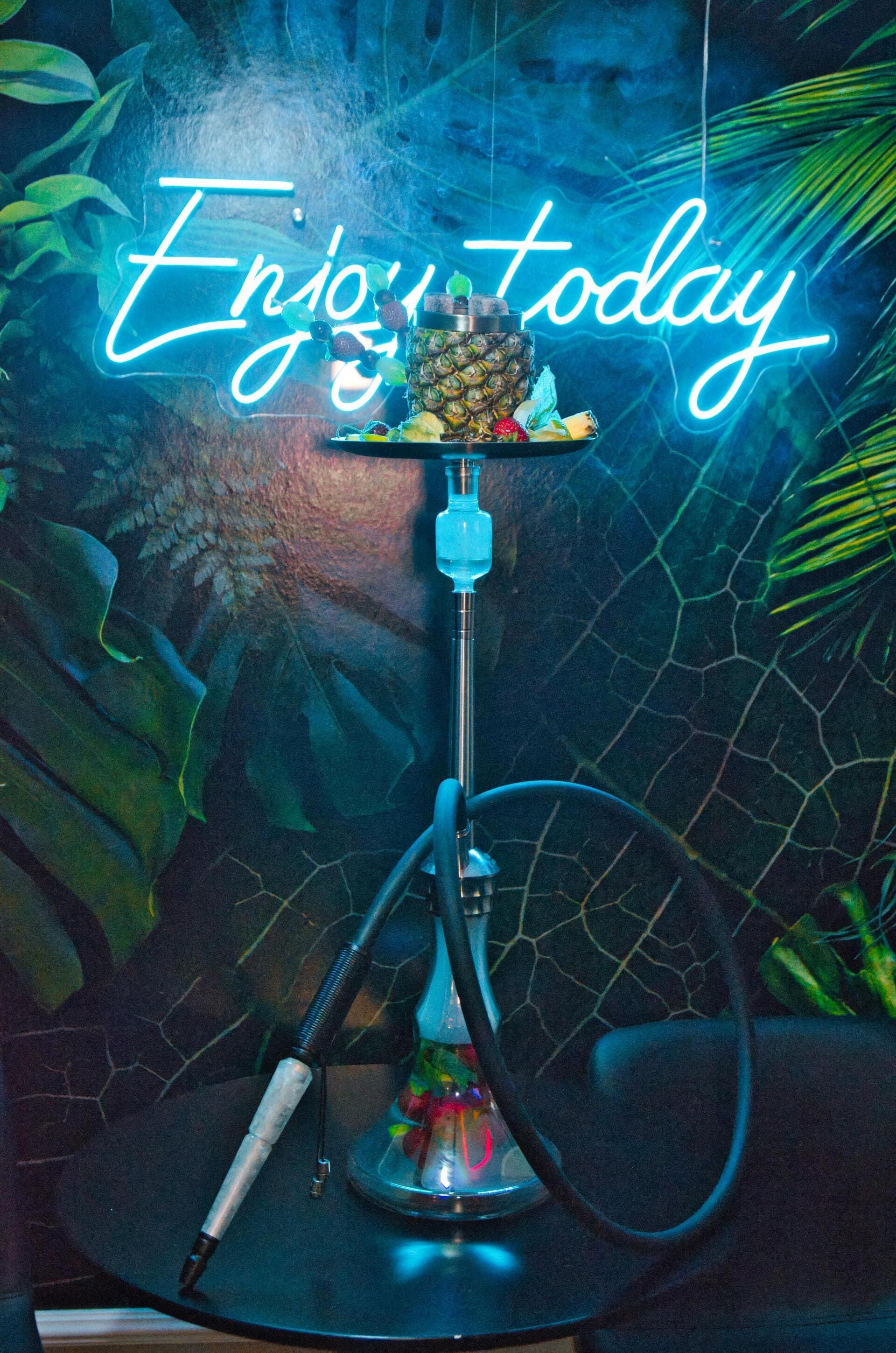 Eine Wasserpfeife sitzt auf einem Tisch vor einem Neonschild | By Mikey