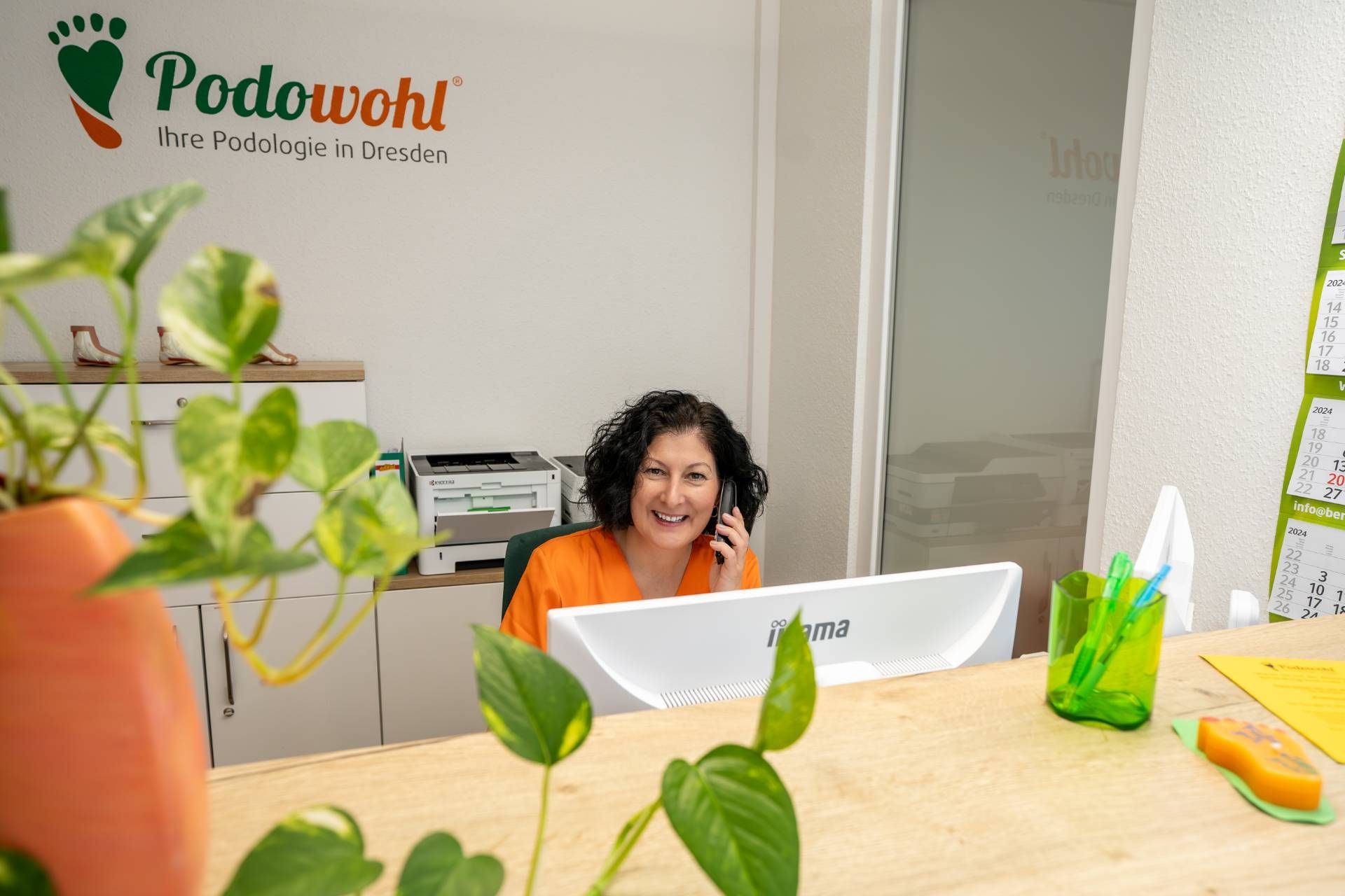 Mitarbeiterin sitzt am Empfang mit einem Telefon am Ohr