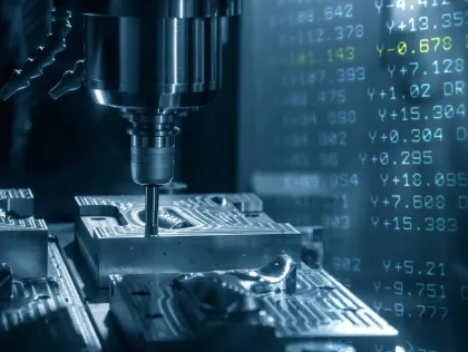 Una máquina está trabajando en una pieza de metal con números en la pantalla detrás de ella.