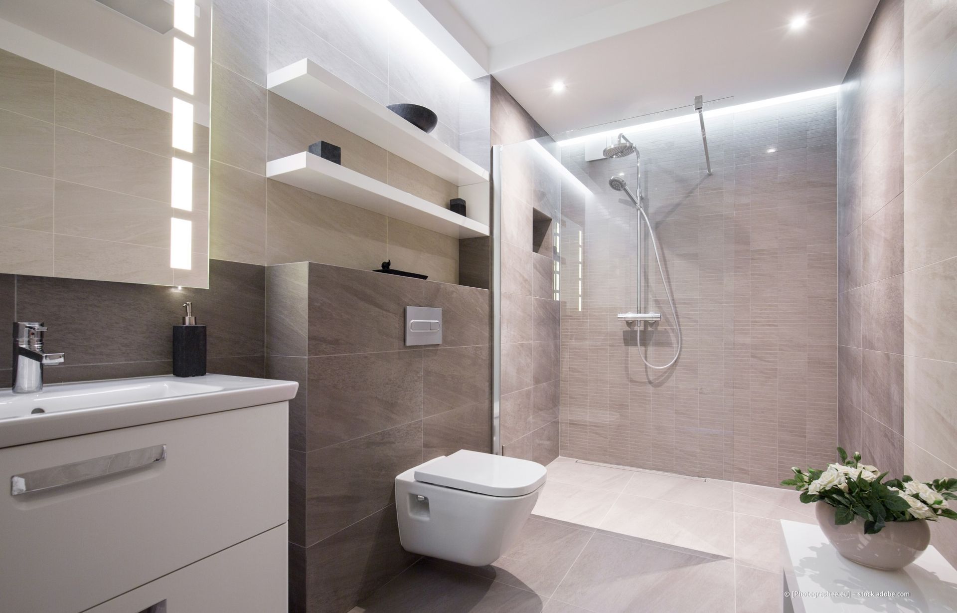 Klempner repariert eine Toilette in einem modernen Badezimmer; der Mann trägt einen grünen Overall.