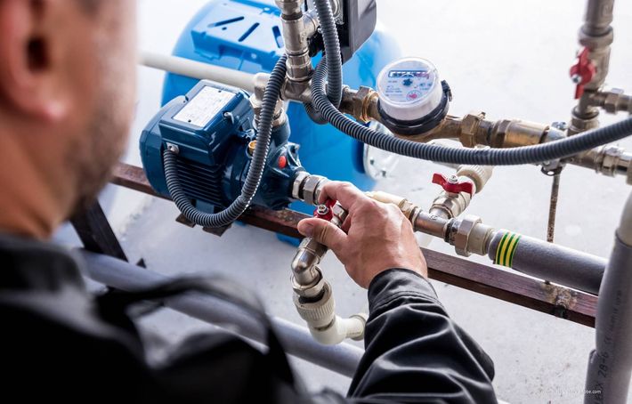 Person, die Rohre an einem blauen Wasserpumpensystem in einem Gebäude einstellt.