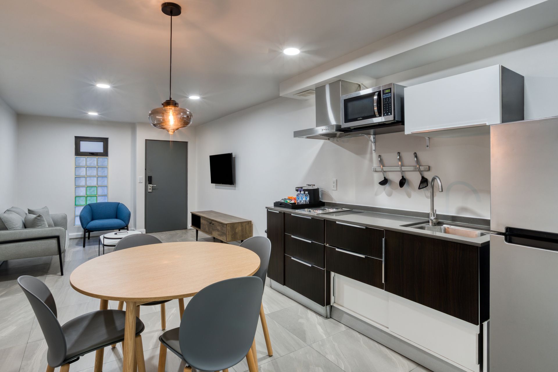 A modern open-concept apartment with a kitchen, a green sofa in the living area, and a dining table in the foreground.