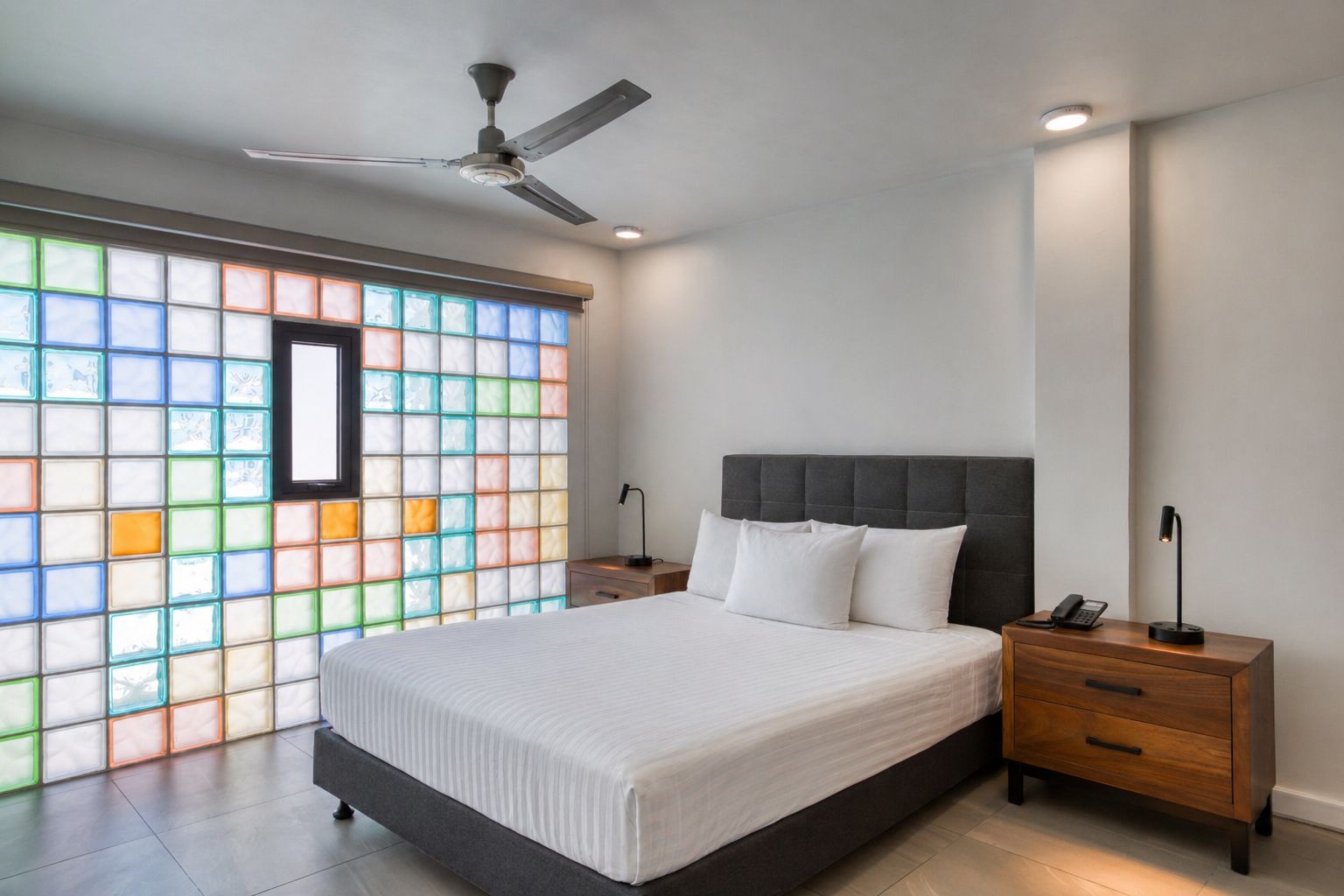 A modern bedroom with a dark tufted headboard, two pendant lights, and a wooden closet, opening into a dining area.