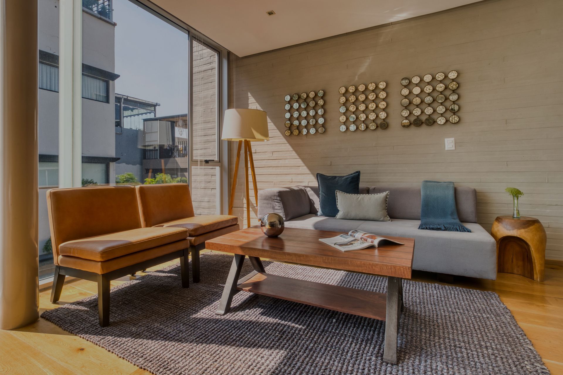 Living room with tan leather seating, grey sofa, wooden table, large window.