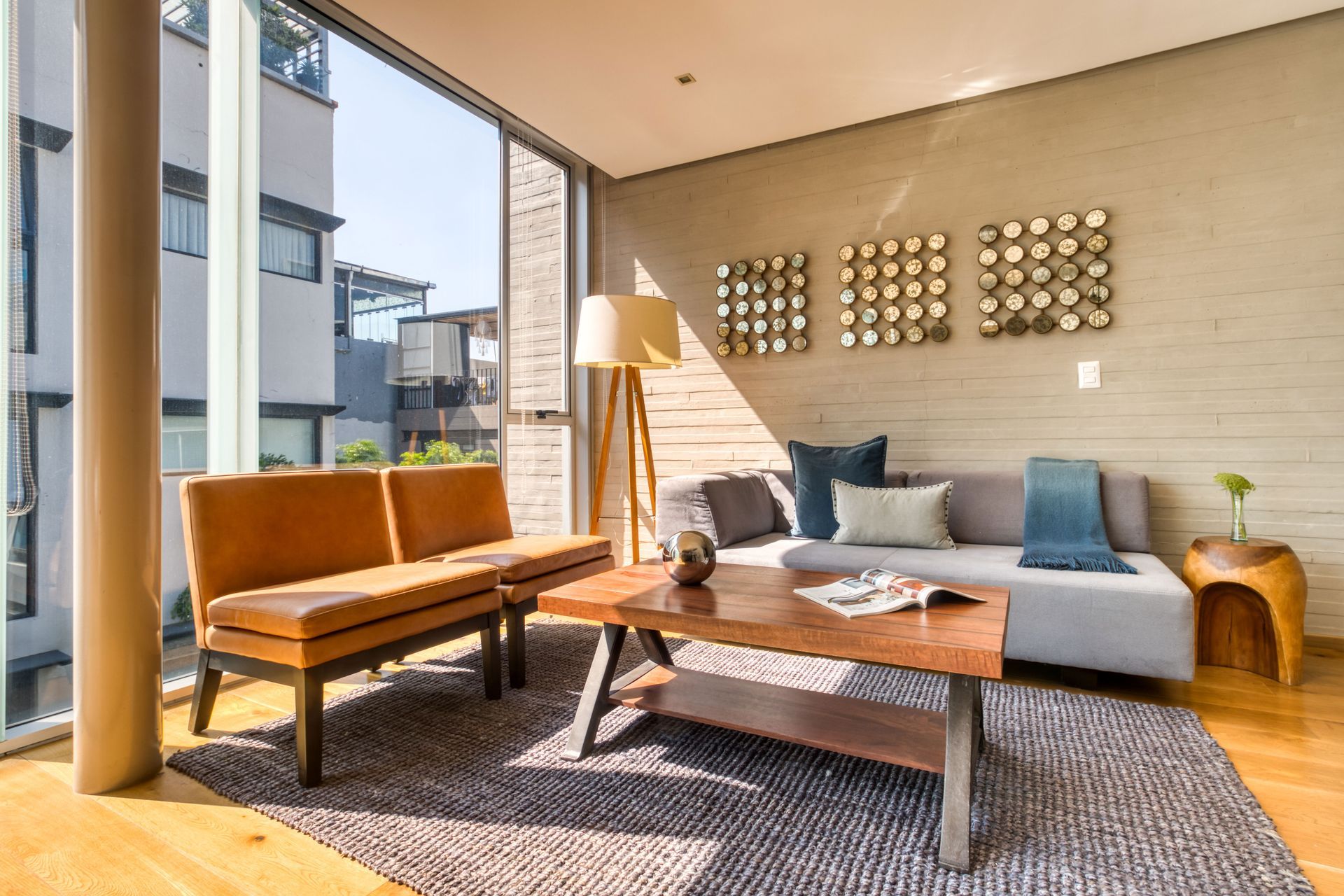 Living room with tan leather seating, grey sofa, wooden table, large window.