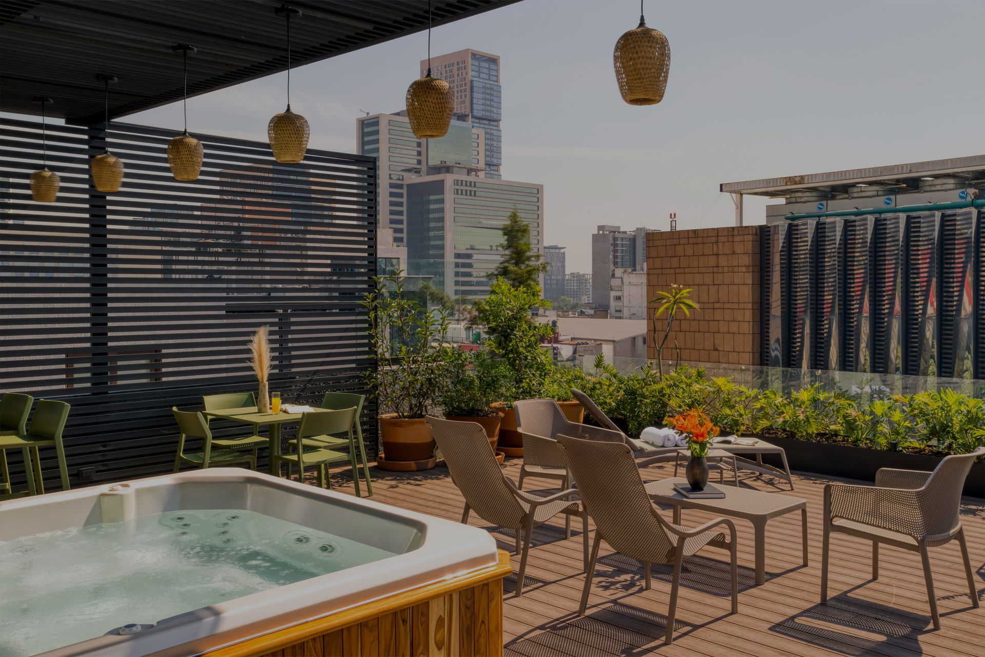 Rooftop patio with jacuzzi, chairs, and cityscape view. Sunny day with plants and hanging lights.