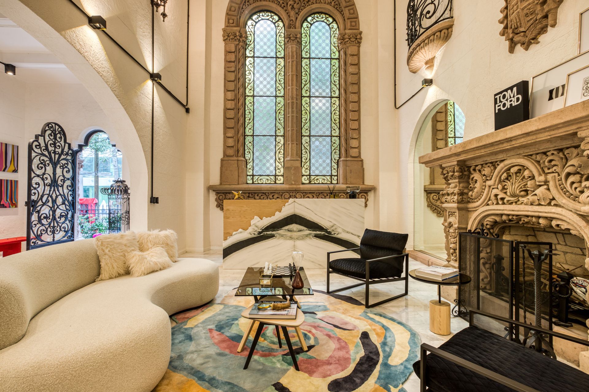 Living room with arched windows, ornate fireplace, curved sofa, and colorful rug.