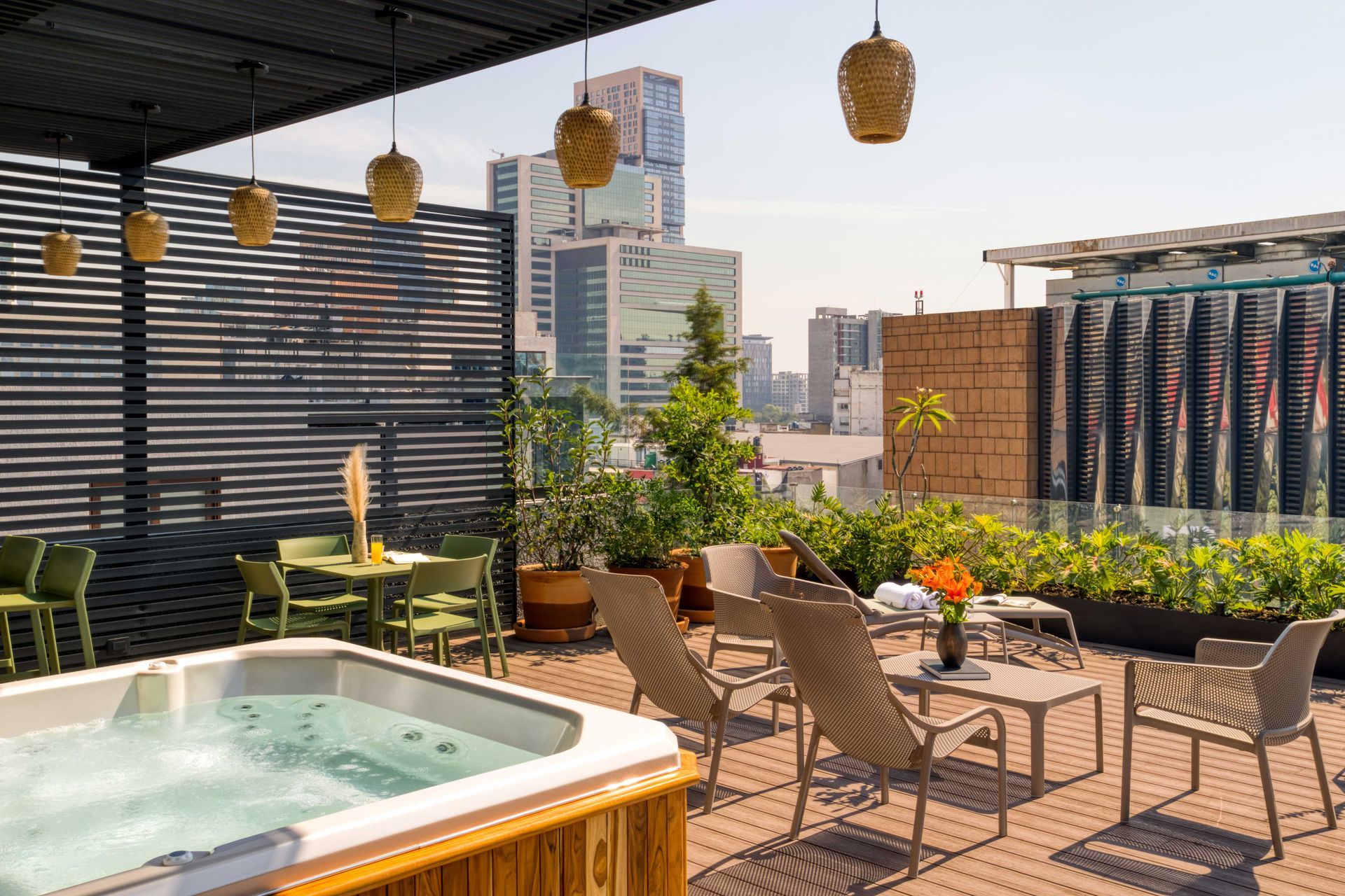 Rooftop patio with jacuzzi, chairs, and cityscape view. Sunny day with plants and hanging lights.