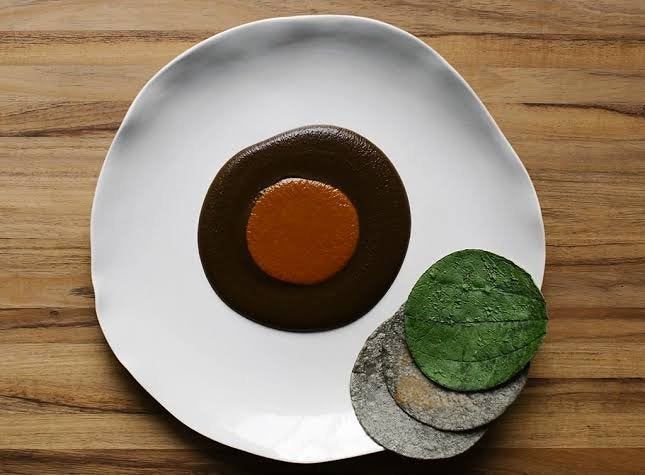 Mole sauce with a red center, three colorful tortillas on a white plate.
