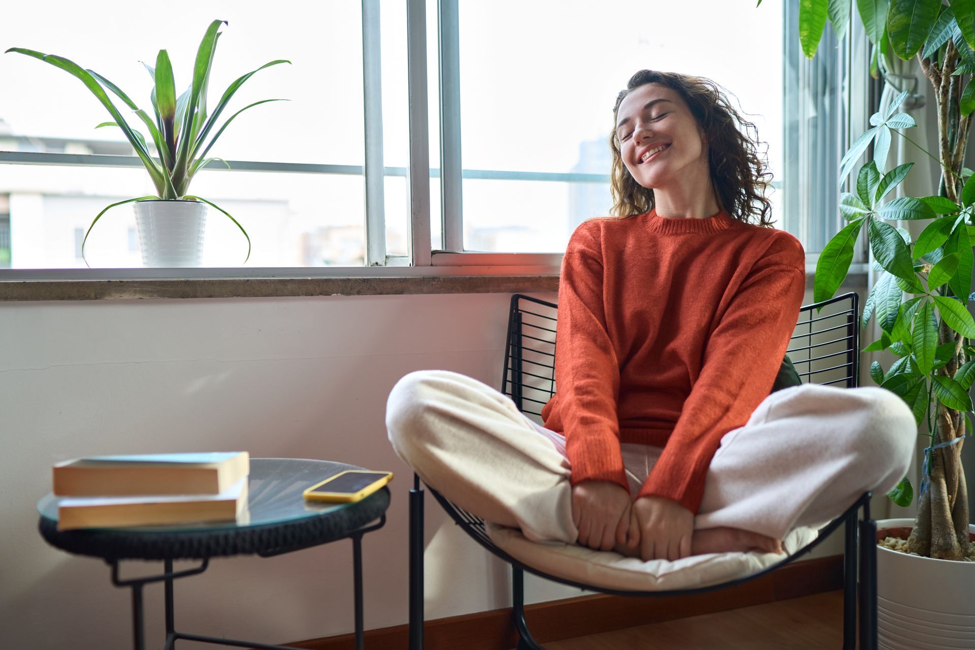 Jeune femme détendue et souriante se relaxant assise sur une chaise à la maison.