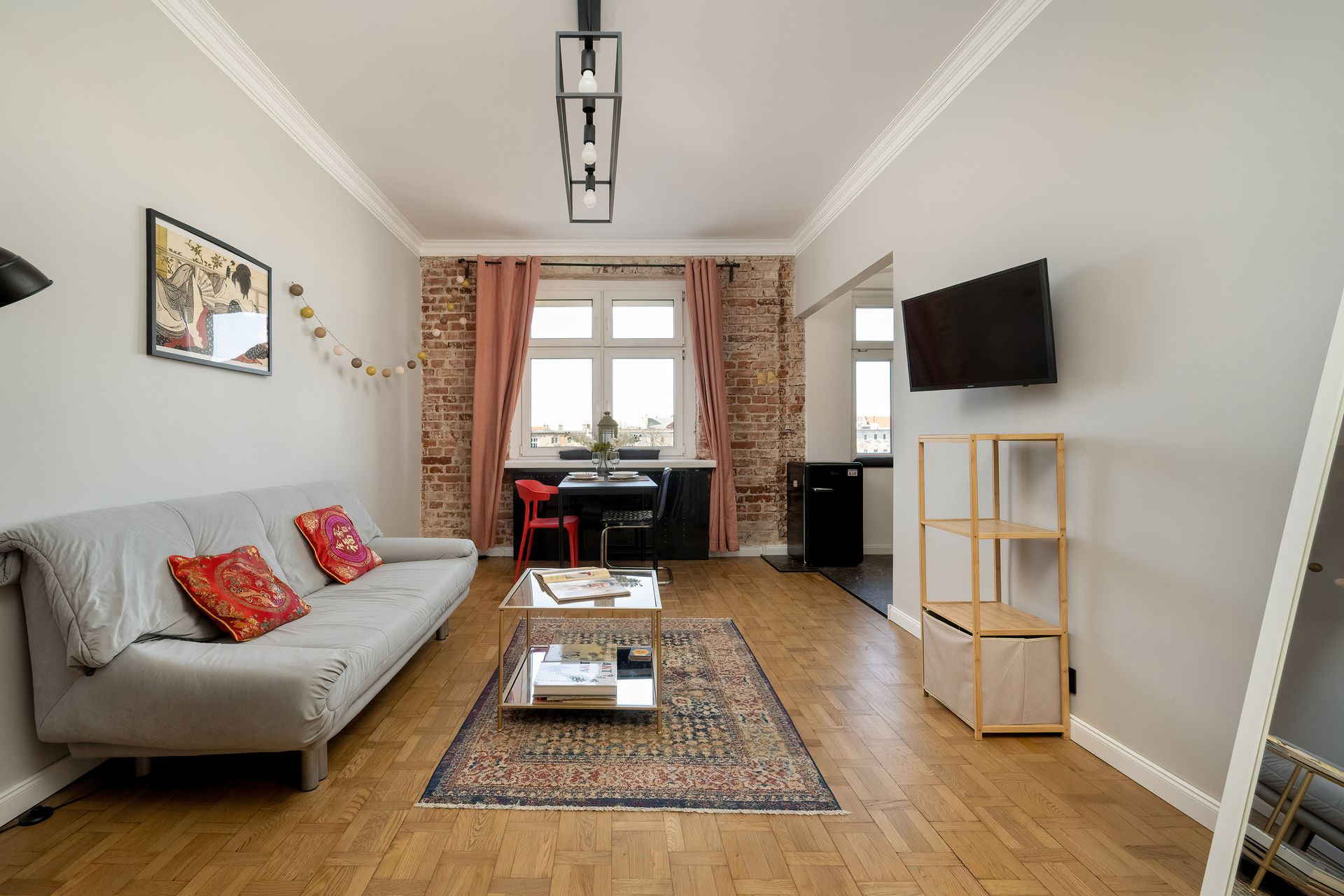 Salon z szarą sofą, dywanem, telewizorem, drewnianą podłogą i widoczną jadalnią.